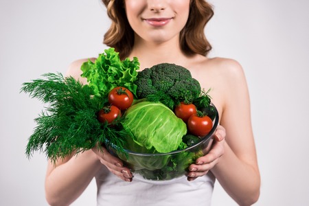 Happy girl posing with bowl of vegetables isolated on white background.の写真素材