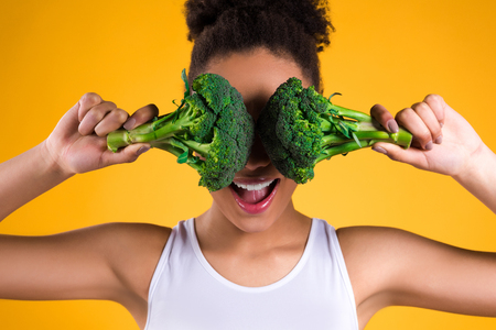African American girl holding broccoli isolated on yellow background.の写真素材