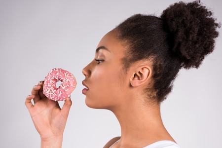 African American girl eating donut isolated on white background.