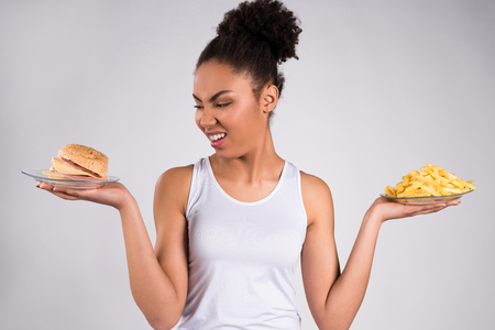 Black girl holding cheeseburger and fries isolated on white background.の写真素材