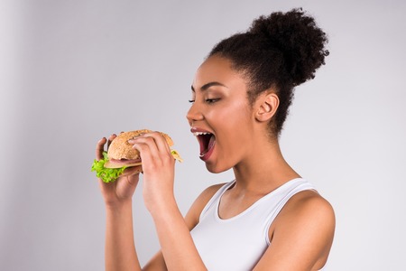 African American girl eating hamburger isolated on white background.