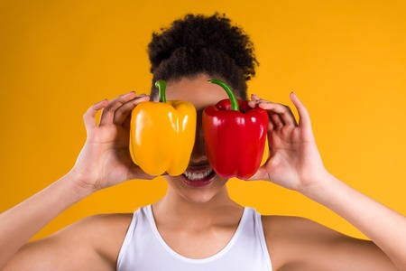 African American girl holding peppers isolated on yellow background.の写真素材