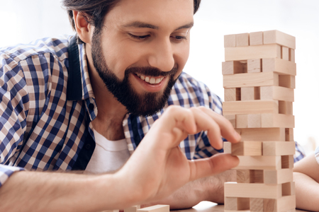 Close up. Smiling bearded man removes wooden blocks from tower.  Fun leisure.の写真素材