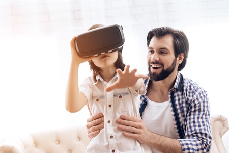 Teenage son uses virtual reality glasses next to father. Future Technology Concept. Interactive...