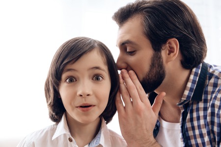 Bearded man tells secret to ear of teenager. Adult father shares secret with son. Gossip.の写真素材
