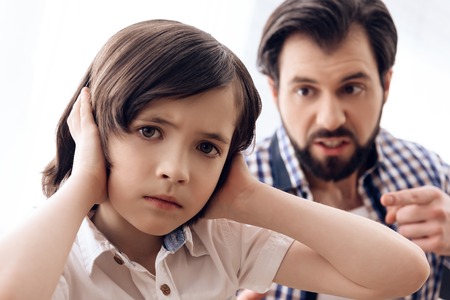 Irate father scolds teenage son which plugs ears. Parenting children concept. Paternity concept.