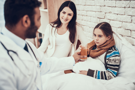 Indian doctor in white gown seeing patients at home. Doctor is giving mixture to girl with pregnant mother.の写真素材