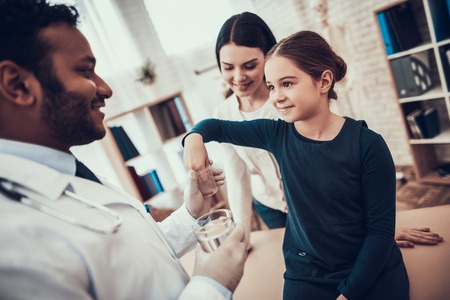 Indian doctor in white gown seeing patients in office. Doctor is giving pills and water to daughter.の写真素材