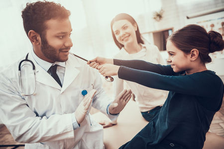Indian doctor in white gown seeing patients in office. Daughter is pulling stethoscope.の写真素材