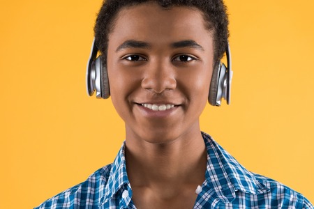 Portrait of happy afro american teen in headphones. Isolated on yellow background. Studio portrait.の写真素材