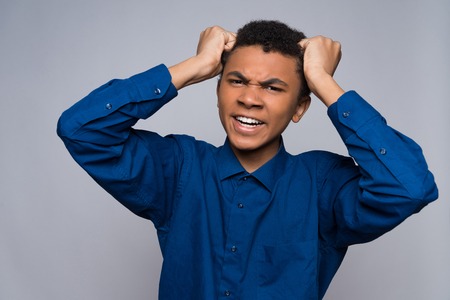 Annoyed African American teenager is tearing hair on head. Isolated on gray background. Studio portrait.の写真素材