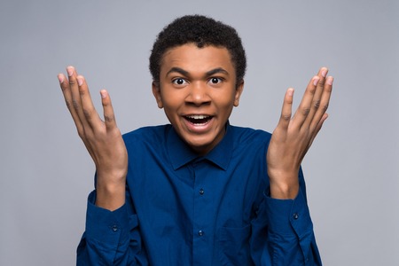 Distraught African American teenager makes helpless gesture. Isolated on gray background. Studio portrait.の写真素材