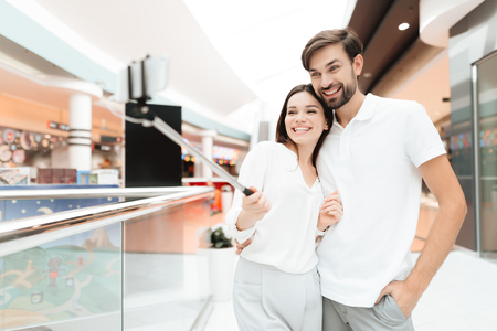 Man and woman in shopping mall. Couple is taking selfie with selfie stick. Couple is smiling.の写真素材
