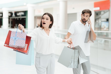 Man and woman with shopping bags are walking to another store in shopping mall. Man is talking on phone.の写真素材