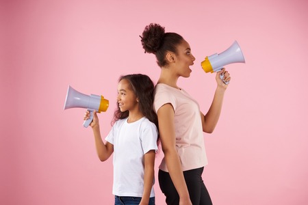 African American woman and little girl are broadcasting in megaphone. Isolated on pink background. Studio portrait.の写真素材
