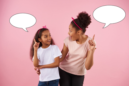 Attractive mother and daughter posing with speech bubbles. Papier mache. Isolated on pink background. Studio portrait.の写真素材