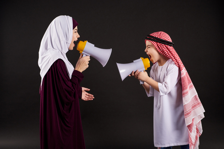 Arab mother and little son in national attire shout in megaphones. Isolated on black background.の写真素材