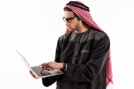 Arab confident businessman in keffiyeh is typing on laptop. Isolated on white background.の写真素材