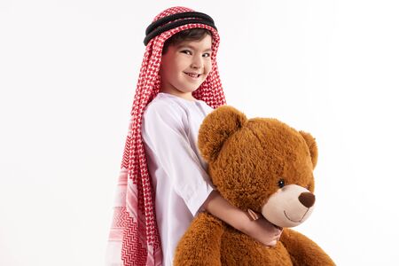 Arabian happy boy in keffiyeh hugs stuffed toy. Childhood concept. Isolated on white background.の写真素材