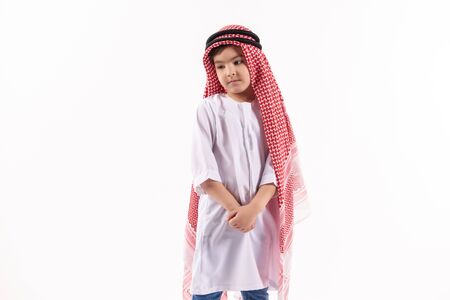 Arabian thoughtful boy in keffiyeh is standing with hands folded. Isolated on white background. Studio portrait.の写真素材