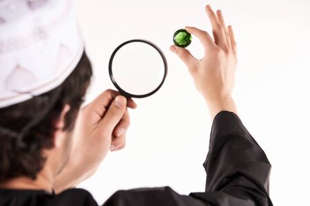 Arab jeweler examines precious stone through magnifying glass. Pawnshop concept. Isolated on white background.の写真素材