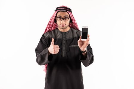 Happy Arab businessman in keffiyeh talks on cellphone and showing thumbs up. Cellular technology concept. Isolated on white background.の写真素材