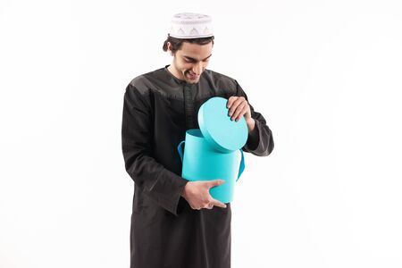 Arab man in ethnic clothes looks in blue box. Isolated on white background. Studio portrait.の写真素材