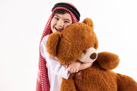 Arabian happy boy in keffiyeh hugs stuffed toy. Childhood concept. Isolated on white background.の写真素材