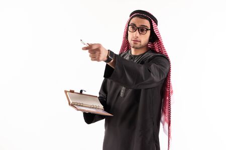 Arab man in keffiyeh makes notes in notebook. Isolated on white background. Studio portrait.の写真素材