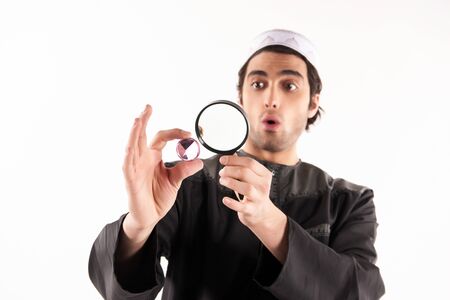Arab jeweler examines precious stone through magnifying glass. Pawnshop concept. Isolated on white background.の写真素材