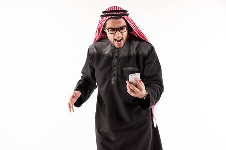Angry Arab businessman in keffiyeh screams on cell phone. Concept of aggression in work. Isolated on white background.の写真素材