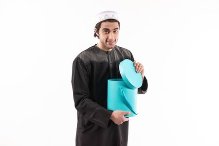 Arab man in ethnic clothes looks in blue box. Isolated on white background. Studio portrait.の写真素材