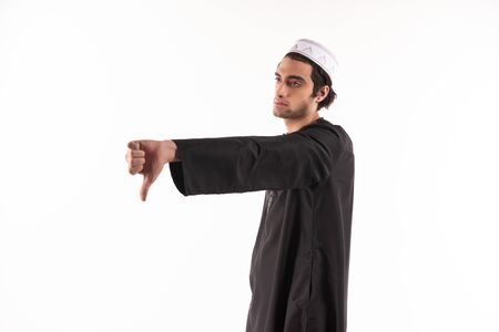 Happy Arab man in ethnic clothes shows thumb down. Isolated on white background. Studio portrait.の写真素材