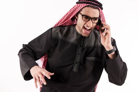 Angry Arab businessman in keffiyeh screams on cell phone. Concept of aggression in work. Isolated on white background.の写真素材