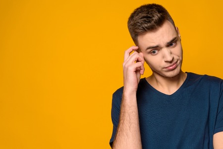 Young handsome guy stands in perplexity isolated on yellow background. Studio portrait. Male...