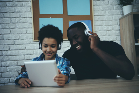 Black teen boy in headphones listening to music with father. Selection of songs in player. Fatherhood.の写真素材