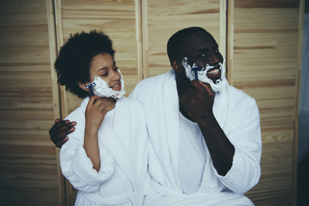 African American man in bathrobe teaches son to shave in bathroom. Men traditions. Two generations. Father Day.の写真素材
