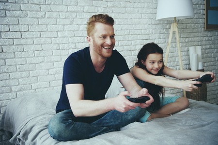 Happy bearded father and teen daughter with joysticks playing video game. Family leisure concept. Fatherhood.の写真素材