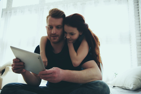 Red haired father and teen daughter are looking at computer tablet. Child education concept. Family leisure.の写真素材