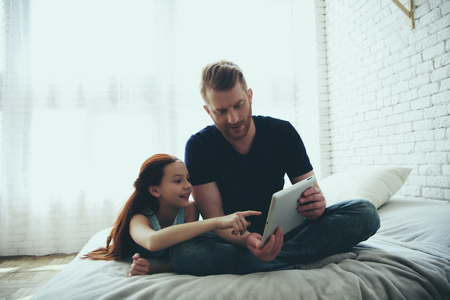 Red haired father and teen daughter are looking at computer tablet. Child education concept. Family leisure.の写真素材
