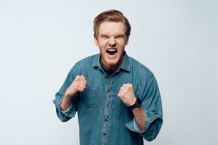 Portrait Euphoric Ecstatic Guy Celebrating Success. Handsome Ginger Bearded Pensive Caucasian Man Screaming and Clenching Fists. Isolated on Light Blue Background. Concept of Human Emotionsの写真素材