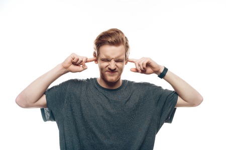 Portrait of Frustrated Man Holding Fingers in Ears. Ginger Serious Young Guy in Casual Clothes has Denial Face Expression Isolated on White Background. Concept of Human Emotionsの写真素材