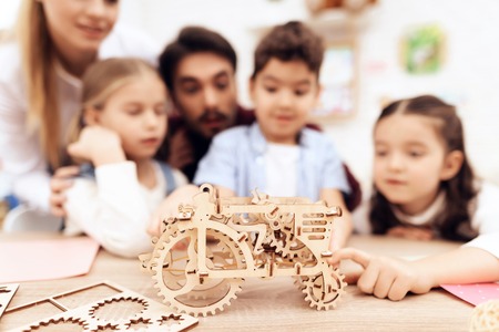 Children collect 3D puzzle - a tractor. At the table are two girls and a boy. A man and a woman help them.の写真素材