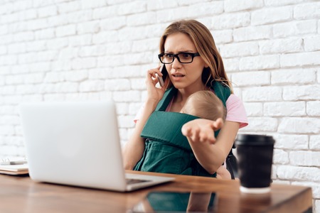 Tired business woman with newborn try to work. Business, motherhood concept.の写真素材