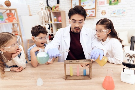 Children together with the teacher for chemistry lessons. They put on goggles and make experiments.の写真素材