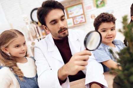 Children together with the teacher look through a magnifying glass on a plant. They have a lesson in biology school.の写真素材