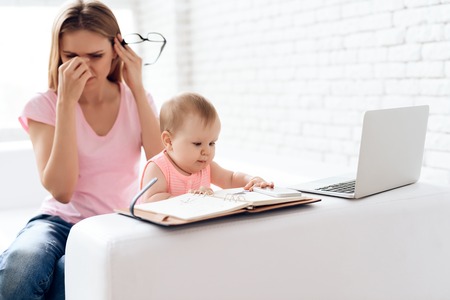 Tired mother with baby working and using laptop. Motherhood concept.の写真素材