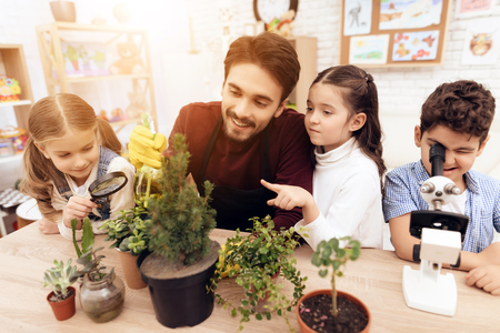 Children together with the teacher look through a magnifying glass on a plant. They have a lesson in biology school.の写真素材