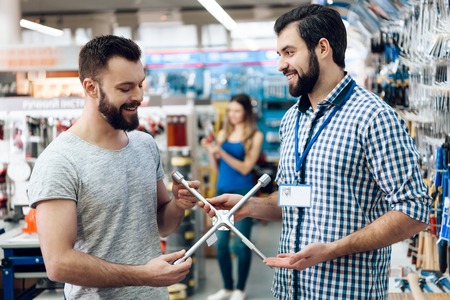 Salesman in checkered shirt is showing bearded client new spanners in power tools store.の写真素材