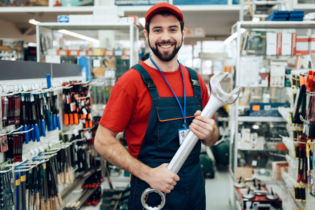 Salesman in red shirt and baseball cap is posing with new giant wrench in power tools store.の写真素材